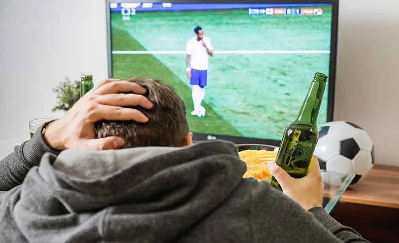 Man kijkt voetbal op ESPN met een fles bier in zijn hand